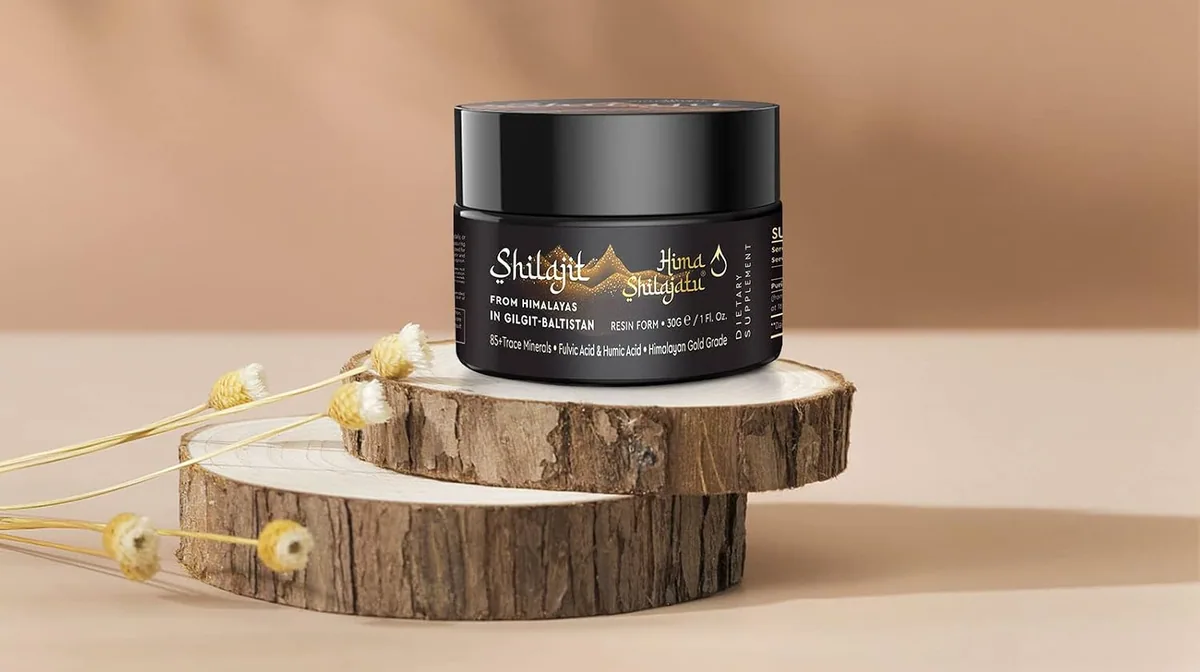 A jar of Hima Shilajatu shilajit resin on two slices of wood against a sand-colored wall